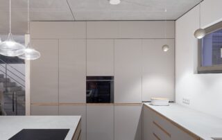 moderner Koch Essbereich mit rohen, ehrlichen Materialien. Sichtbetondecke, Industrieestrich und als Kontrast, natürlicher, weiß geölter Eiche-FischgrätParkett. Die Eiche-Elemente sind wiederholen sich in Ausbaudetails , Möbel und Küche. Der Küchenblock schwebt und hat metallisch champagnerfarbene Fronten. Die Fronten der Küche sind in einem dezenten warmen grau gehalten. Griffleisten sind auf weiß pigmentierter Eiche bündig Eingesetz. Die Arbeitsplatte ist ein hellgrauer keramischer dünner Kunststein.