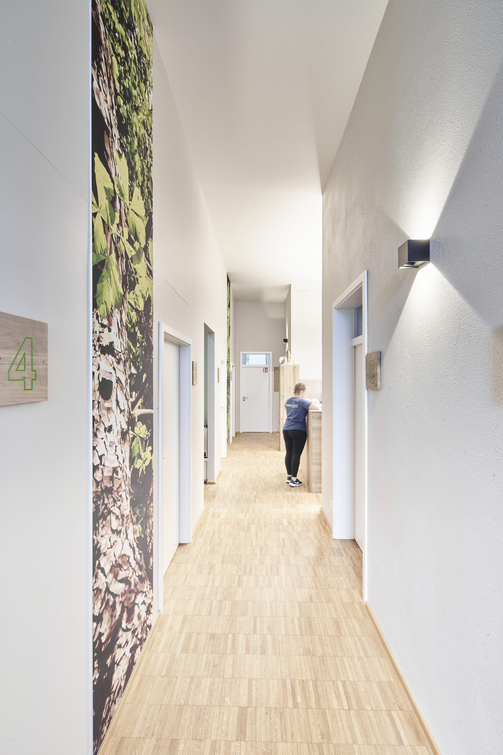 Innenansicht Praxis für Physiotherapie, Flurbereich mit raumhohen Bannern. Parkettboden und passende Oberflächen in dezentem grau und weiß geölter Eiche
