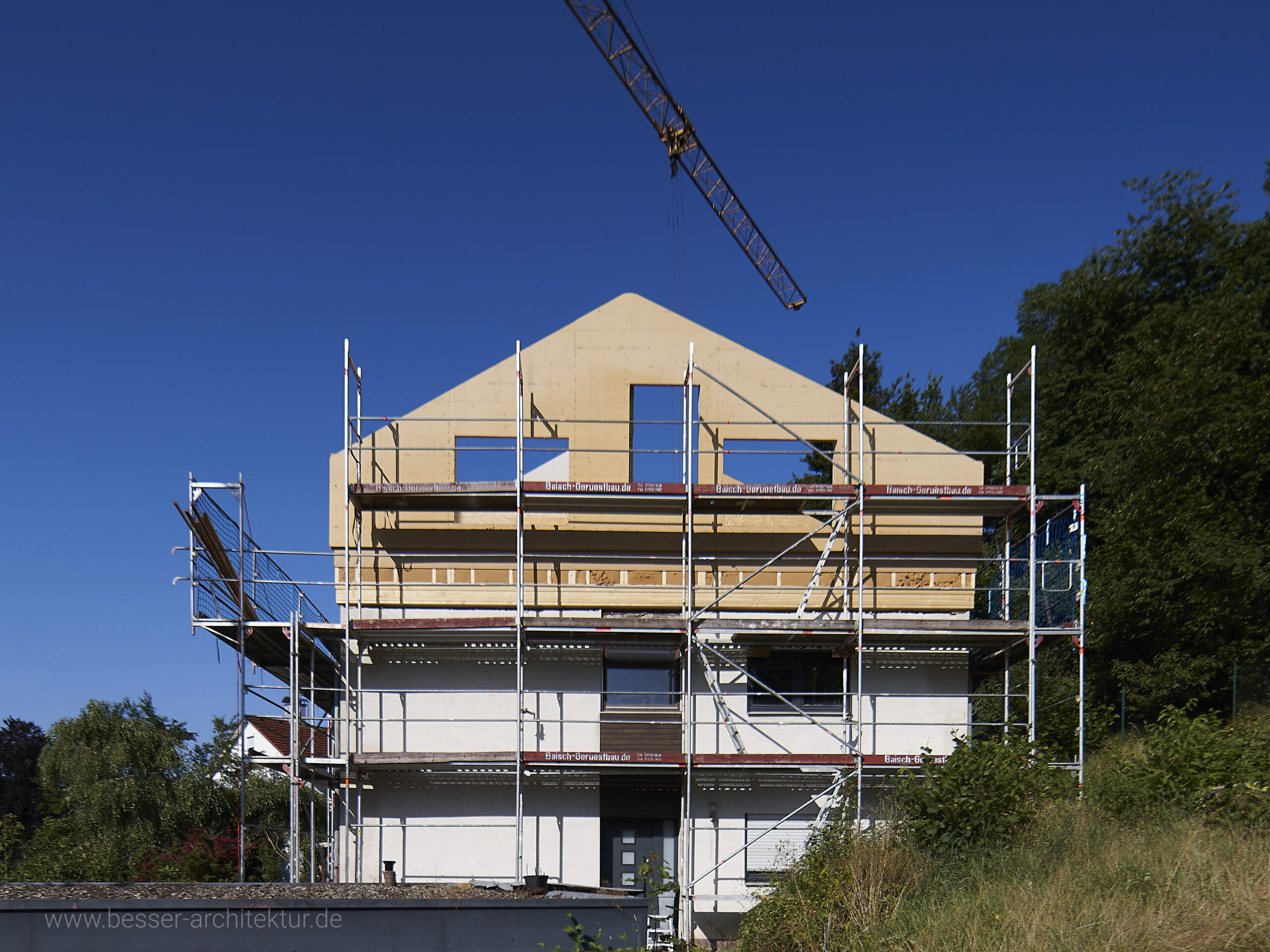 Aufstockung eines bestehenden Wohnhauses mit einer kompletten Wohnung. Aufrichtung der vorgefertigten Holzkonstruktion, Brettstapeldecke, Holz-Ständerwände, noch alles im rohen Zustand. Kran und blauer Himmel bei Sonnenschein