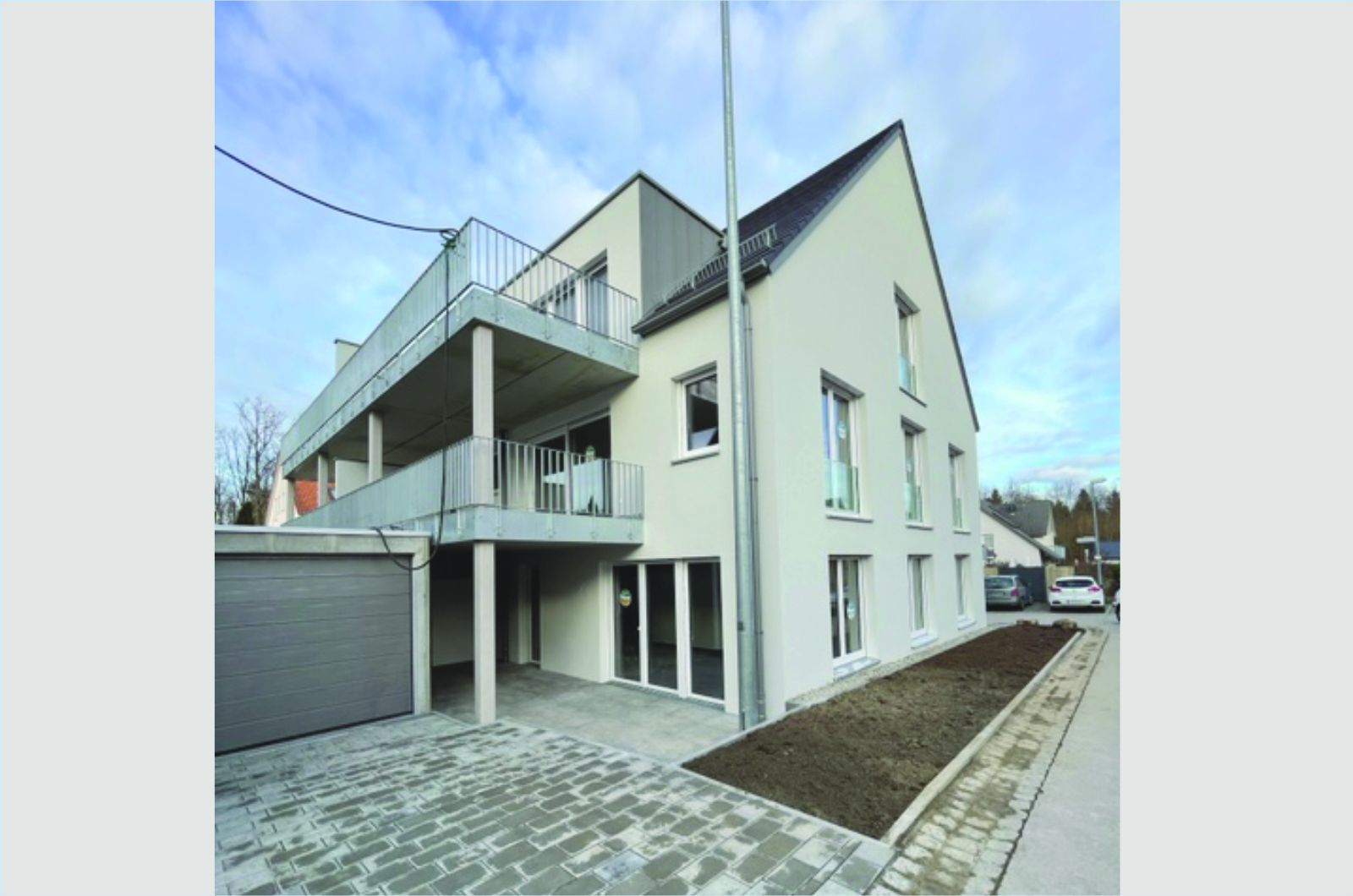 Mehrfamilienhaus mit Sichtbeton im unteren Bereich, darüber weiß verputzt und mit Satteldach und Garage